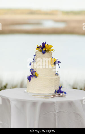 three tiered wedding cake with flowers at outdoor reception Stock Photo