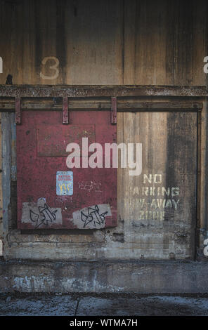 A closed red door on the exterior of an old industrial building that says 'No Parking Tow Away Zone' Stock Photo