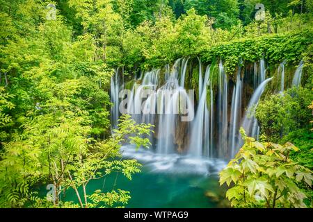 A long exposure nature scene, with beautiful silky waterfalls dropping into an emerald green pool, surrounded by lush vegetation.