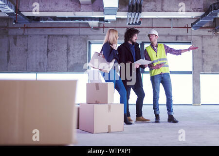 architect using tablet computer while showing house design plans to a young couple at construction site Stock Photo