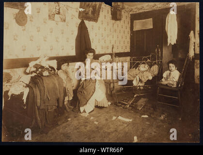 Mrs. Guadina, living in a rear house at 231 Mulberry St. N.Y., a dirty poverty-stricken home, and making a pittance by finishing pants. On the trunk is the work of four days. She was struggling along, (actually weak for want of food) trying to finish this batch of work so she could get the pay. There seemed to be no food in the house and she said the children had had no milk all day. The father is out of work (sells fish) on account of rheumatism. Three small children and another expected soon.  Photographs from the records of the National Child Labor Committee (U.S.) Stock Photo
