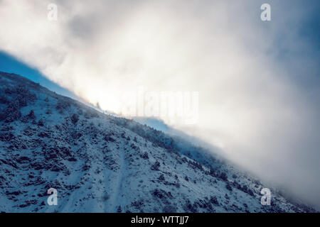 Dramatic pictersque landscape of snowy winter mountains partially covered by clouds with cold winter sun Stock Photo