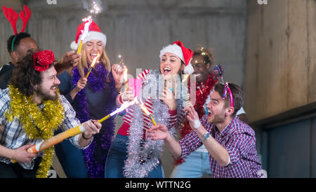 multiethnic group of young happy casual business people dancing with sparklers and having fun while celebrating new year eve in front of concrete wall Stock Photo