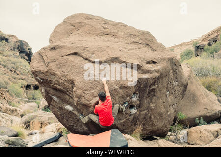 Man in red tshirt climbing a boulder Stock Photo