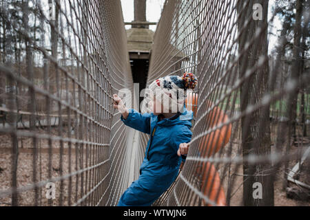 young boy looking through a net thinking at an outdoors playground Stock Photo