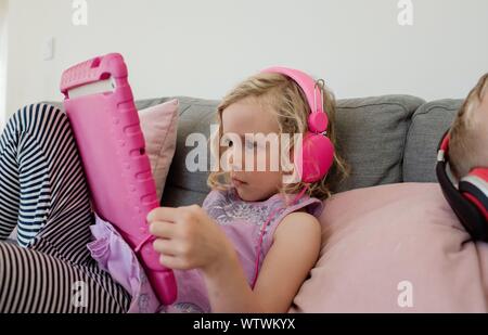young girl sat at home looking at an iPad with headphones on Stock Photo