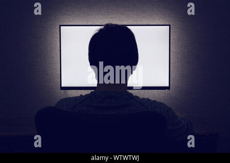 Man sits in front of a blank monitor in dark room Stock Photo
