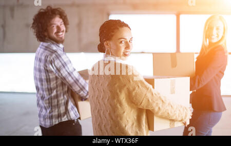 happy young casual business team carrying cardboard boxes with sunlight through the windows during moving in at new unfinished startup office building Stock Photo
