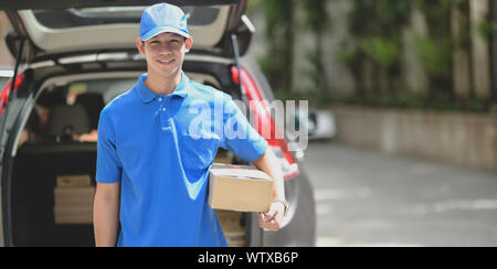 Delivery man preparing parcel box to customer and smiling to the camera while standing in front of his car Stock Photo