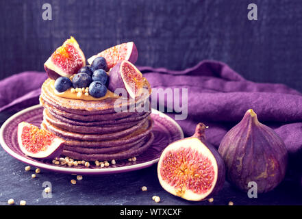 Healthy lilac pancakes with chokeberry and acai powder topped with peanut butter with figs and blueberries Stock Photo