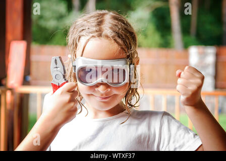 Young girl holding toy pliers and wearing glasses raising clenched fist in sign of success. Stock Photo