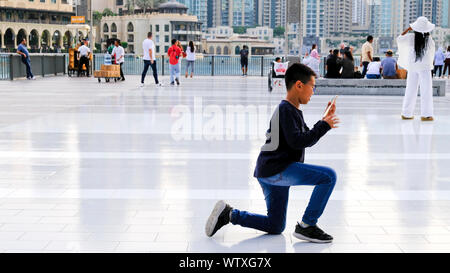 Dubai, United Arab Emirates - 31 October, 2018: Tourist are gathering on the Dubai mall square. A young Asian boy is kneeling to take a picture. Stock Photo