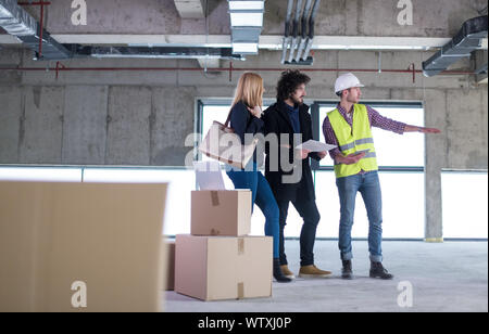 architect using tablet computer while showing house design plans to a young couple at construction site Stock Photo