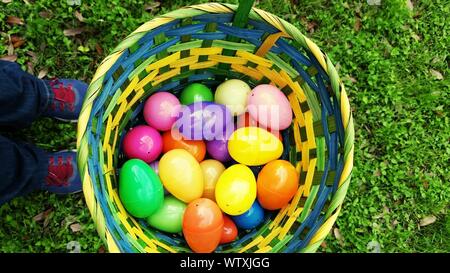 Low Section Of Child Standing By Easter Eggs In Basket On Field