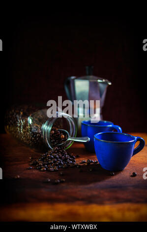 Two Mediterranean blue traditional coffee cups with coffee beans tumbling from a jar.