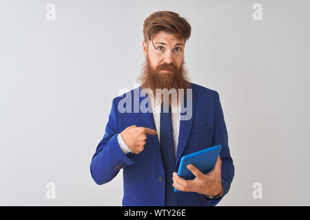 Young redhead irish businessman using tablet over isolated white background with surprise face pointing finger to himself Stock Photo