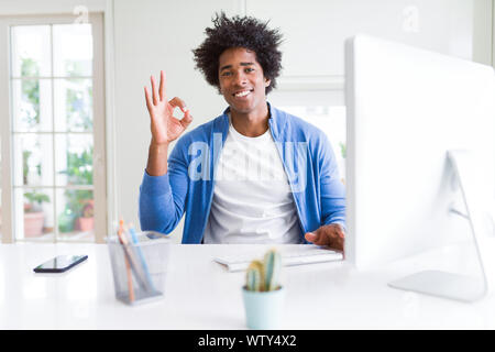 African American man working using computer doing ok sign with fingers, excellent symbol Stock Photo