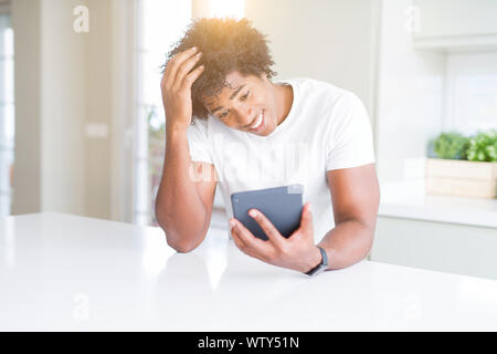African American man using touchpad table stressed with hand on head, shocked with shame and surprise face, angry and frustrated. Fear and upset for m Stock Photo