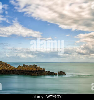Square format view of a rocky cliff outcrop in a calm ocean under an expressive sky on the Emerald Coast in France Stock Photo