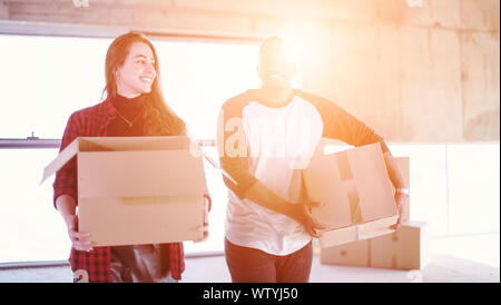happy young multiethnic casual business team carrying cardboard boxes with sunlight through the windows during moving in at new unfinished startup off Stock Photo