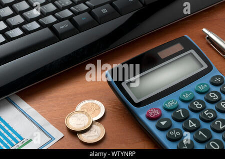 Calculator on wooden table with a pen and some euro coins in front of a black computer keyboard Stock Photo
