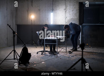 videographer recording young talented hacker while working on laptop computer in dark office with concrete wall in the background Stock Photo