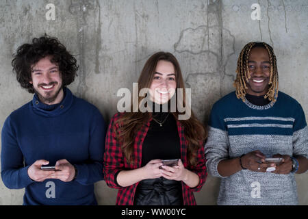 young multiethnic successful casual business team using mobile phones while standing in front of a concrete wall at new startup office Stock Photo