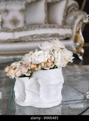 bouquet of delicate pink roses in a cup on the table. Bedside table, interior of a fashion house. Rococo sofa with vase of rose. Luxury rich living ro Stock Photo