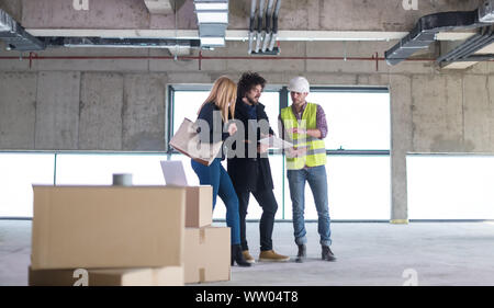 architect using tablet computer while showing house design plans to a young couple at construction site Stock Photo