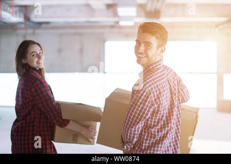happy young casual business team carrying cardboard boxes with sunlight through the windows during moving in at new unfinished startup office building Stock Photo