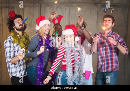 multiethnic group of young happy casual business people dancing with sparklers and having fun while celebrating new year eve in front of concrete wall Stock Photo