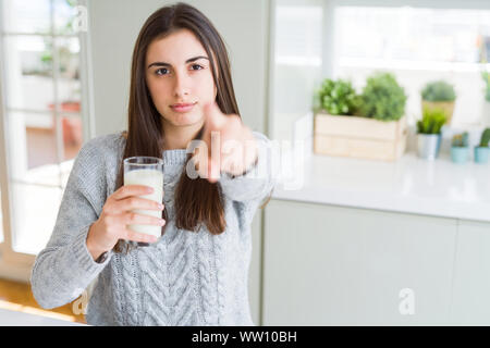 Beautiful young woman drinking a glass of fresh milk pointing with finger to the camera and to you, hand sign, positive and confident gesture from the Stock Photo