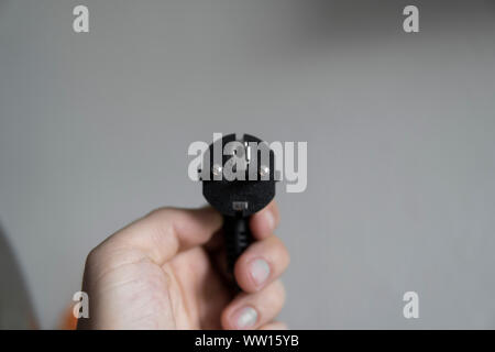 Hand holding black electric plug on a grey background. Stock Photo