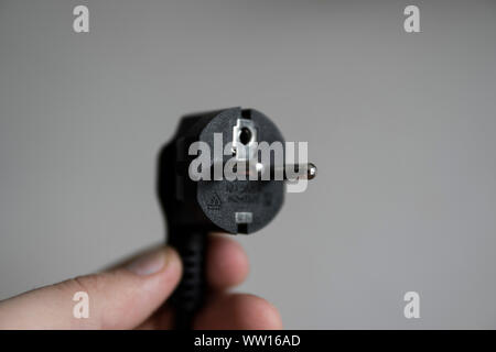 Hand holding black electric plug on a grey background. Stock Photo