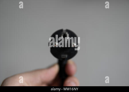 Hand holding black electric plug on a grey background. Stock Photo