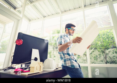 Young caucasian holding his blueprint project at the desk in home office. Stock Photo