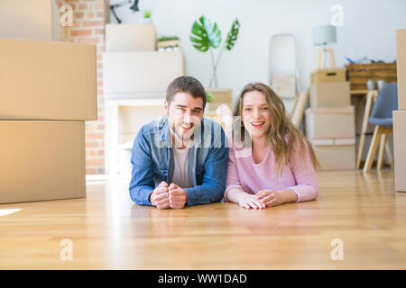 Young beautiful couple in love relaxing lying on the floor together with cardboard boxes around for moving to a new house Stock Photo