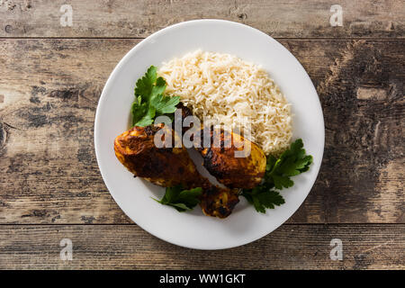 Roasted tandoori chicken with basmati rice in plate on wooden table. Top view. Stock Photo