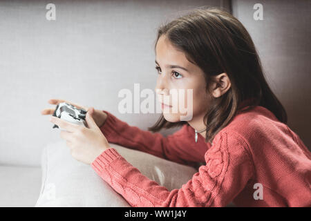 Niña jugando en casa con la videoconsola tumbada en el sofá Stock Photo