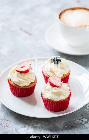 Three vanilla cupcakes with wipped cream and berries on a white plate with cup of cappuccino. Stock Photo