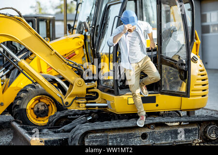 Handsome builder or construction worker getting out of the escavator on the construction site Stock Photo
