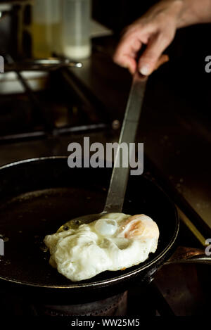 closeup of a woman frying an egg in a frying pan, in a professional kitchen Stock Photo