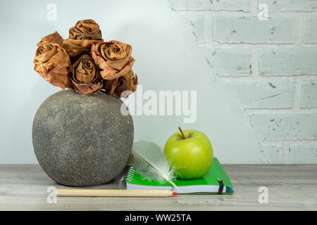 Back to school concept with green spiral ring bound notebook, apple, pencil and quill pen on the table against a white brick wall with free copy space Stock Photo