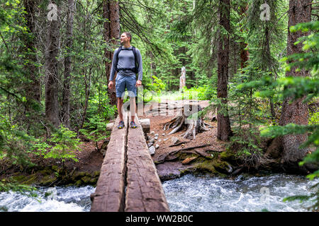 Mountain river stream with man crossing standing in rocky mountains in summer of 2019 on Conundrum Creek trail in Aspen, Colorado with wooden bridge Stock Photo