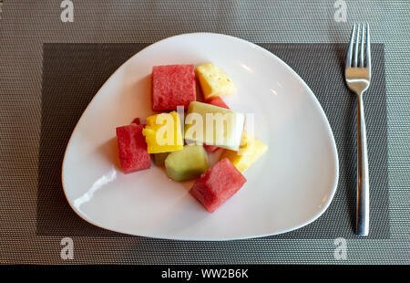 Fruit salad, sliced watermelon, melon and pineapple in squares. Sliced fruits on a plate, top view. Stock Photo