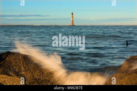 lighthouse in the sea with waves crashing over rocks Stock Photo