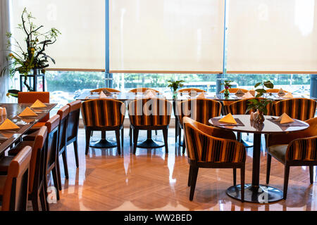 Served tables in the hotel restaurant. The banquet room is ready to receive guests. Roller blinds omitted and a Chinese plant in the corner. Stock Photo