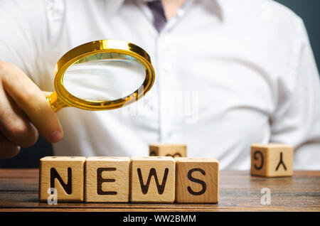 A journalist holds a magnifying glass over the word News. Review the main events and analytics. Fake news. Information. The most important events in t Stock Photo
