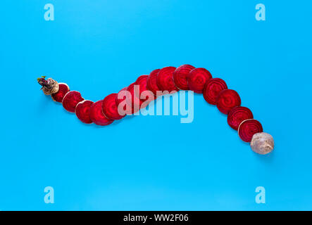 Organic beet diced in slices and arranged in a curved line on a blue tabletop. Above view of fresh beetroot. Winter vegetable concept. Minimal style. Stock Photo