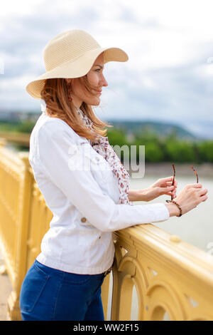 Natural beauty woman in hat smiling on bridge over Danube, profile view, Margaret Bridge, Budapest, Hungary Stock Photo